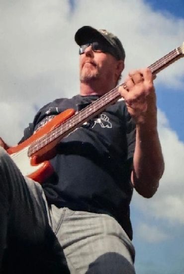 Man playing electric guitar outdoors under blue sky.
