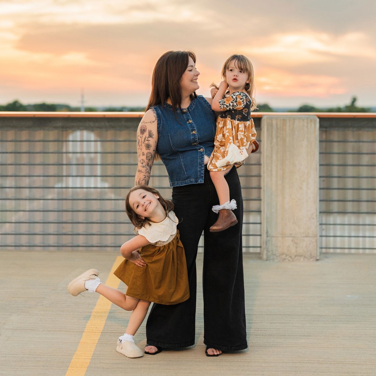 Mother with two young daughters posing playfully on a rooftop at sunset