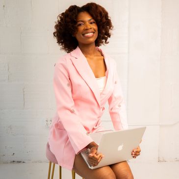 Smiling woman in pink blazer sitting with laptop.