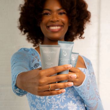 Smiling woman presenting skincare products in blue packaging.
