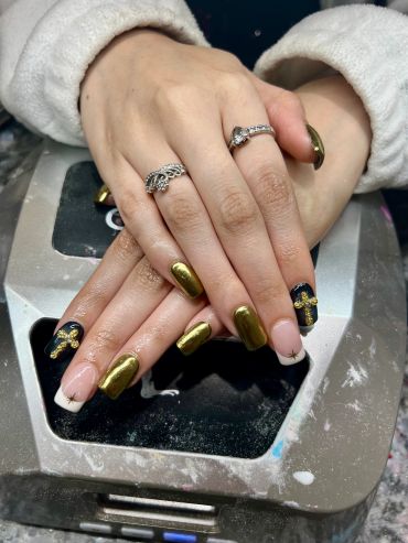 Hands with metallic gold and black cross nail art and silver rings.