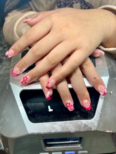 Hands with red floral nail art resting on a metallic surface.