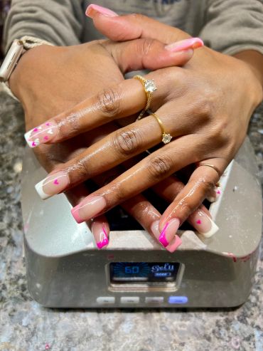 Hands with decorated nails and rings resting on a UV nail dryer.