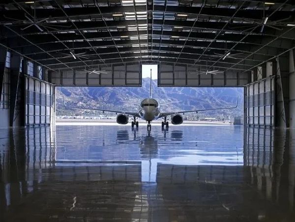 Airplane parked inside a hangar with mountains in the background.