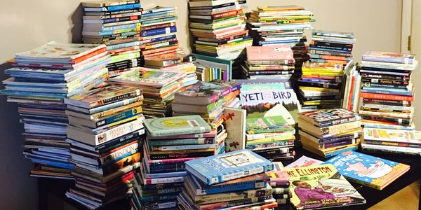 Large stacks of assorted books piled on a table.