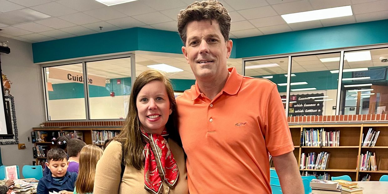 Two adults posing in a library with children in the background.
