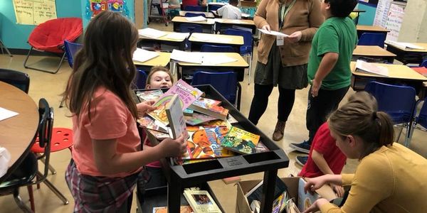 Children and adults sorting books in a classroom.