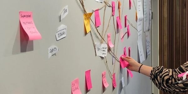 Person arranging pink sticky notes on a wall with interconnected strings and labels.