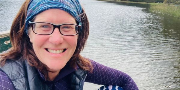 Smiling woman enjoying a peaceful moment by a lake surrounded by trees.