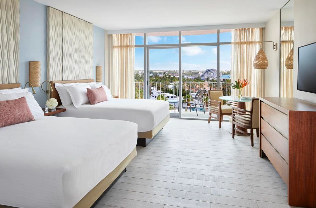 Bright hotel room with two beds and a balcony view of a marina.