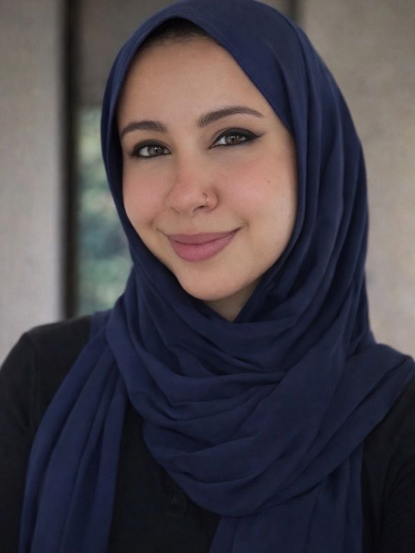 A smiling woman wearing a navy blue hijab and black top.