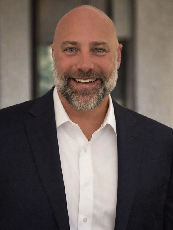 Smiling bald man with a beard in a dark suit and white shirt.