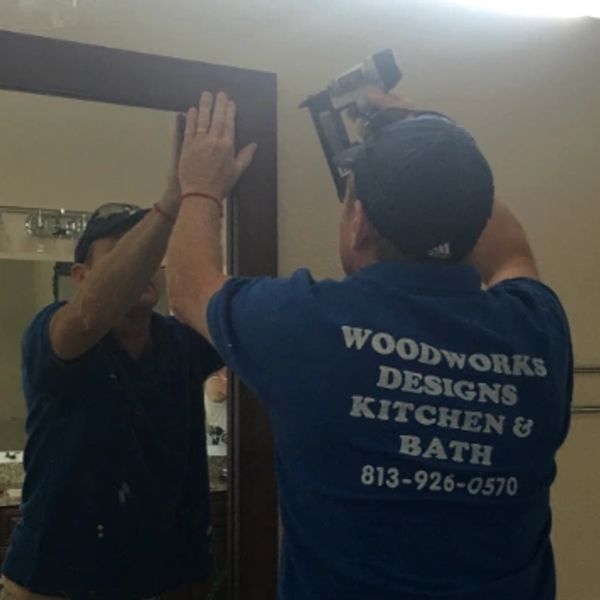 A carpenter installs a mirror frame using a nail gun.