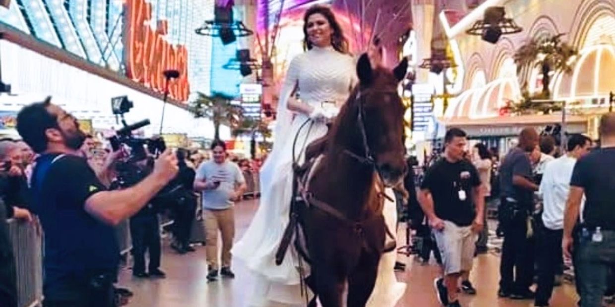 A woman in a white dress rides a horse through a vibrant, crowded street at night.