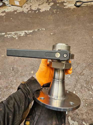 Hand holding a metallic valve with a black handle.