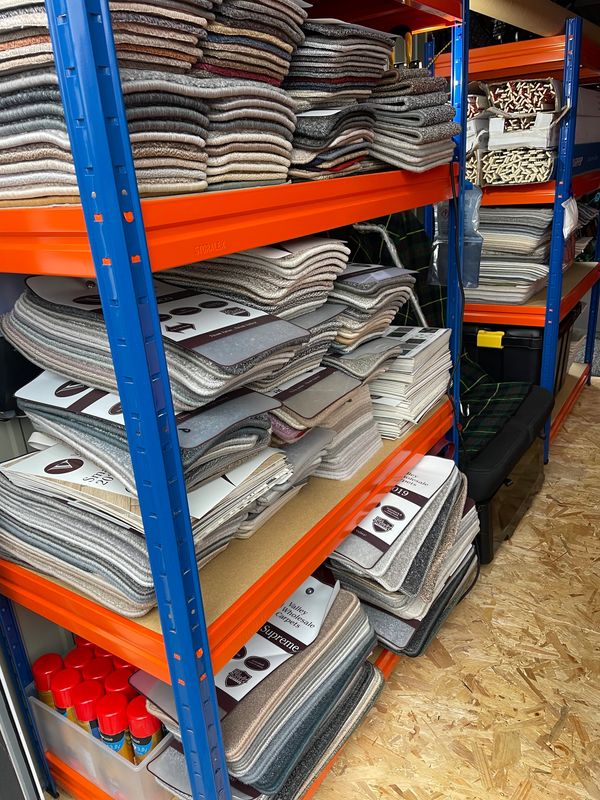 Shelves stacked with folded carpets and spray cans in a storage room.