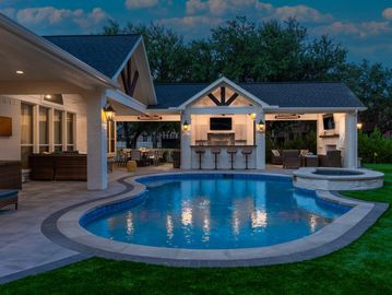 Elegant backyard with a pool, bar seating, and cozy outdoor lounge under soft evening lights.