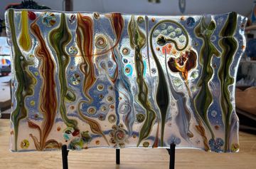 Colorful glass artwork with swirling patterns and organic shapes on a clear rectangular panel.