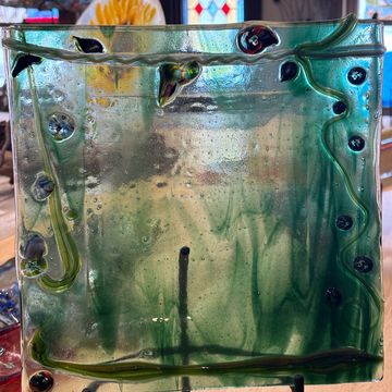 Decorative glass panel with green swirls and embedded shapes on display.