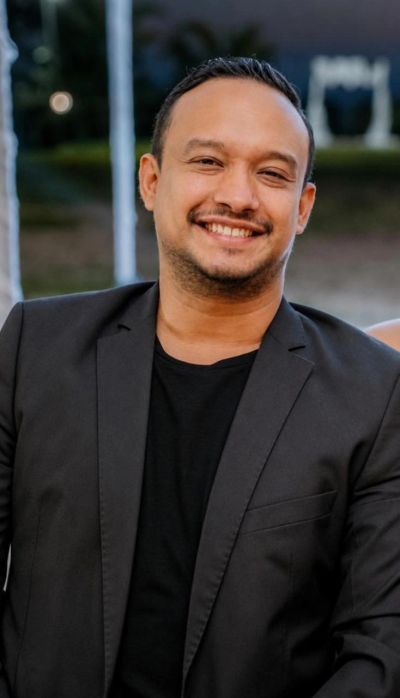 Hombre sonriente con saco negro y camiseta negra.
