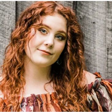 Young woman with curly red hair smiling gently.