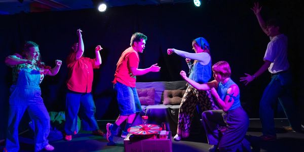 Group of people acting dramatically on a stage with colorful lighting.