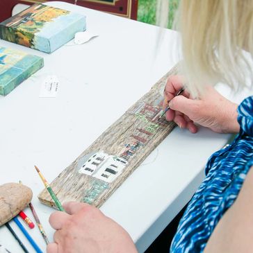 Person painting a detailed miniature scene on a wooden plank.