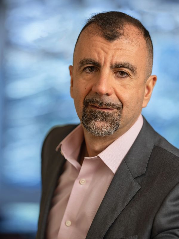 Professional middle-aged man in a suit with a light pink shirt and trimmed beard.