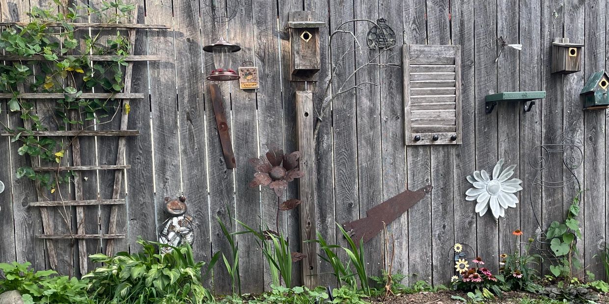 Bird houses, plants, and metal flowers adorn a wooden fence