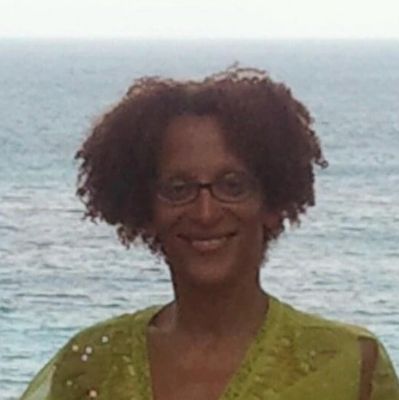 Woman smiling by the ocean wearing glasses and a green top.