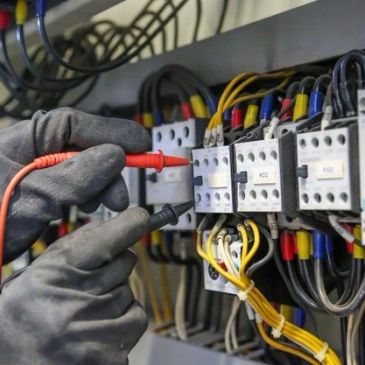Electrician testing electrical connections with probes in a control panel.