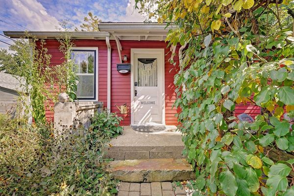 Charming red house entrance with a white welcome door and lush greenery.