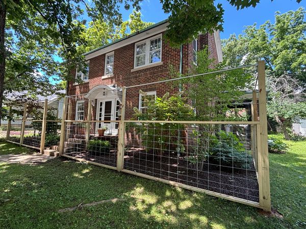 Brick house with a newly installed wire fence and lush greenery.