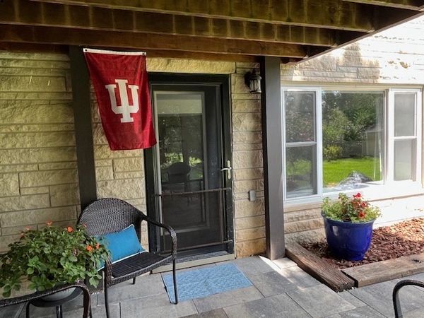 Porch with Indiana University flag, black chair, and potted plants.