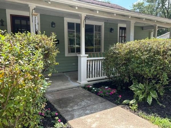 Front porch of a green house with bushes and flowers.