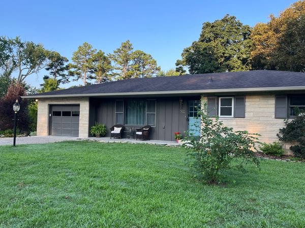 Single-story house with a green lawn and front porch seating under a clear blue sky.