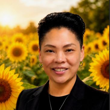 Smiling person with short hair stands in a sunflower field at sunset.