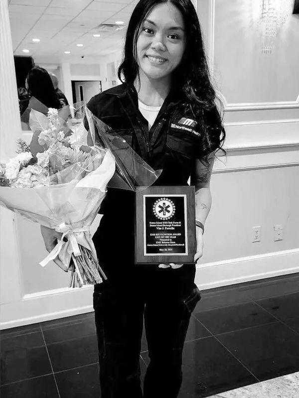 Woman in uniform holding flowers and an award plaque indoors.