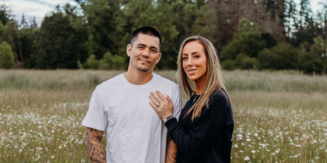 Couple posing outdoors in a field with wildflowers and trees in the background.