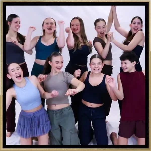 A joyful group of nine young dancers posing and smiling together.