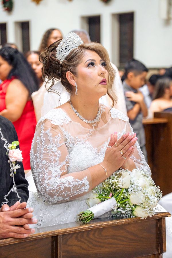 Bride in a white lace dress praying during wedding ceremony.