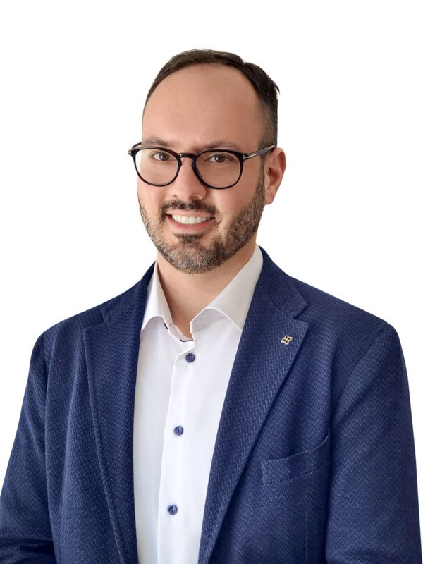 Smiling man in glasses wearing a blue blazer and white shirt.