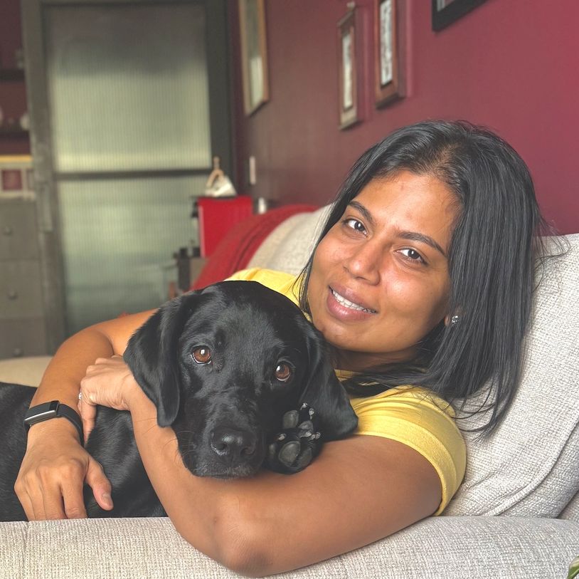 Woman in yellow hugging a black dog on a couch.