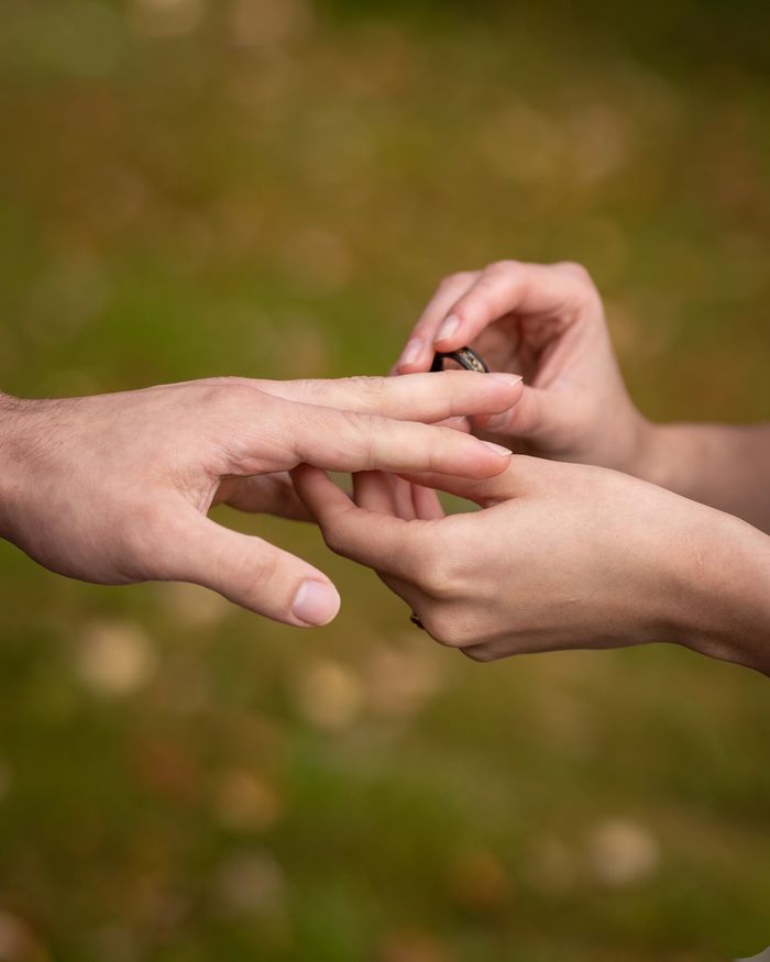 A person placing a ring on another person's finger outdoors.