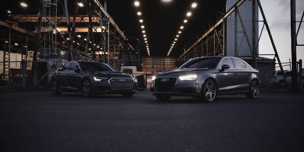 Two sleek black Audi cars parked under industrial lights at night.
