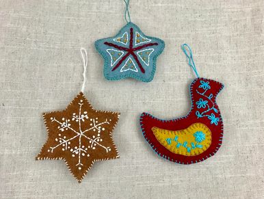 Three colorful felt Christmas ornaments with embroidery, including stars and a bird shape.