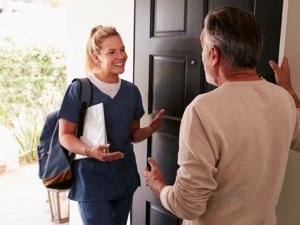 Senior man opening his front door to a female healthcare worker making a home health visit
