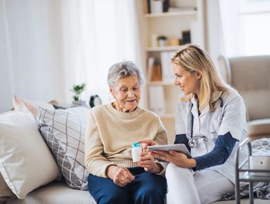 A health visitor with a tablet explaining to an elderly woman how to take pills.
