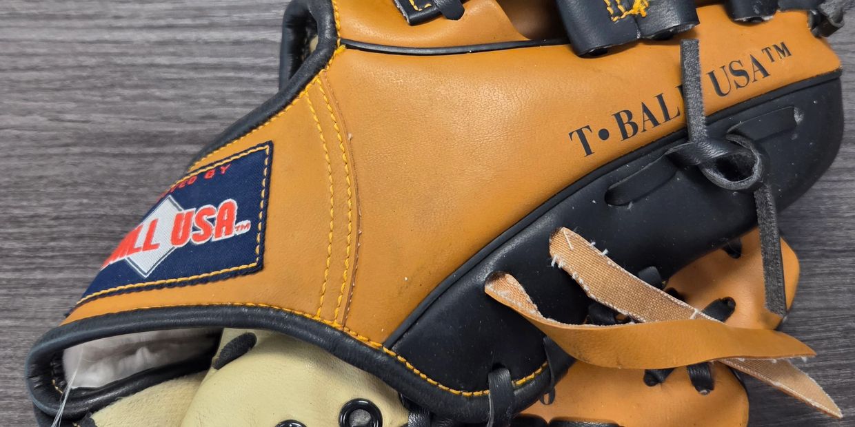 Close-up of a tan and black T-Ball USA baseball glove on a wooden surface.