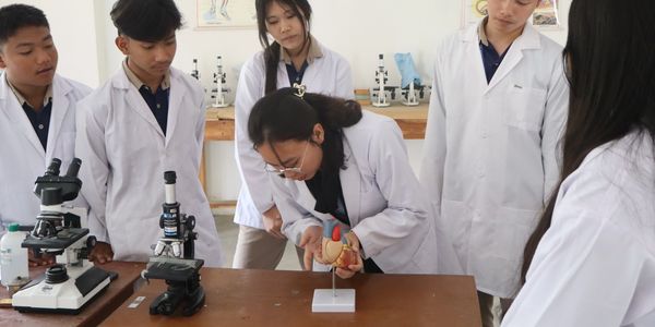 Students in lab coats studying a heart model in a science classroom.